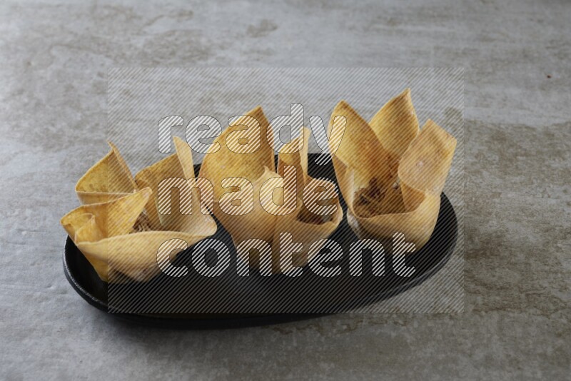 wonton cups on oval black ceramic plate on grey textured counter top