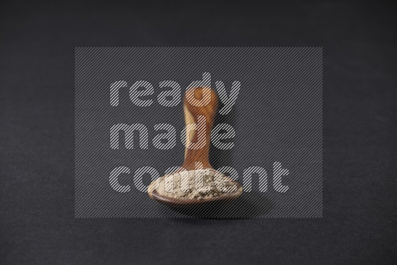 A wooden ladle full of garlic powder on a black flooring