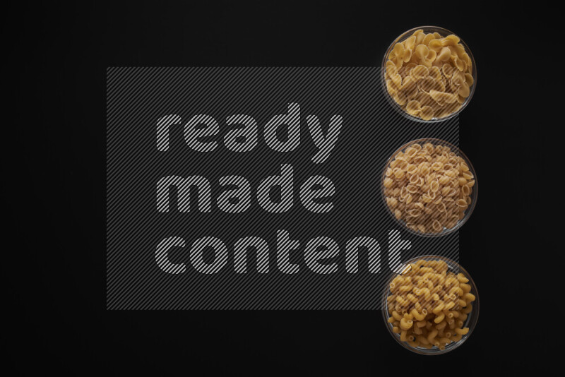 Different pasta types in 3 glass bowls on black background