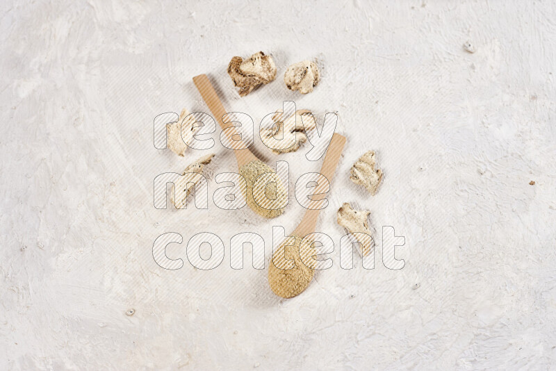 Two wooden spoons full of ground ginger powder on white background