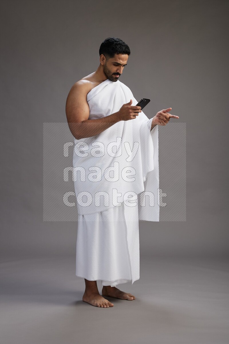 A man wearing Ehram Standing texting on phone on gray background