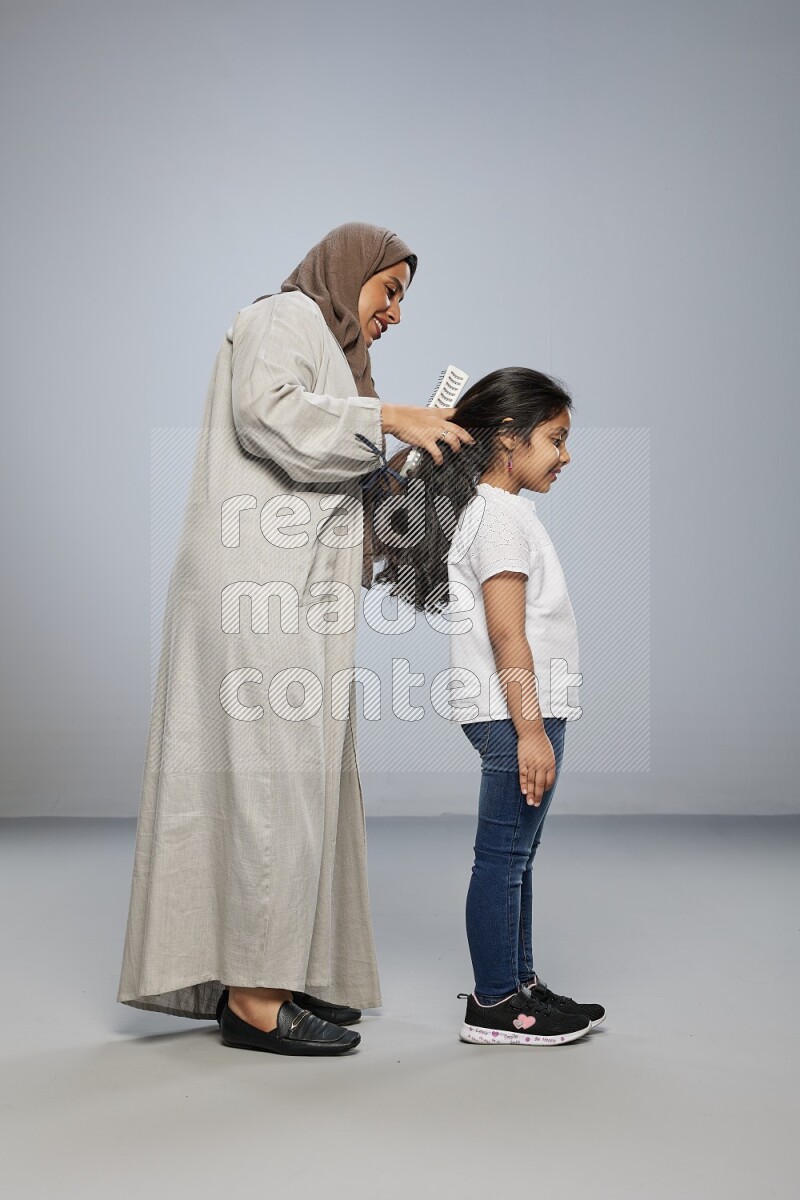 Mom standing styling hair for her daughter on gray background