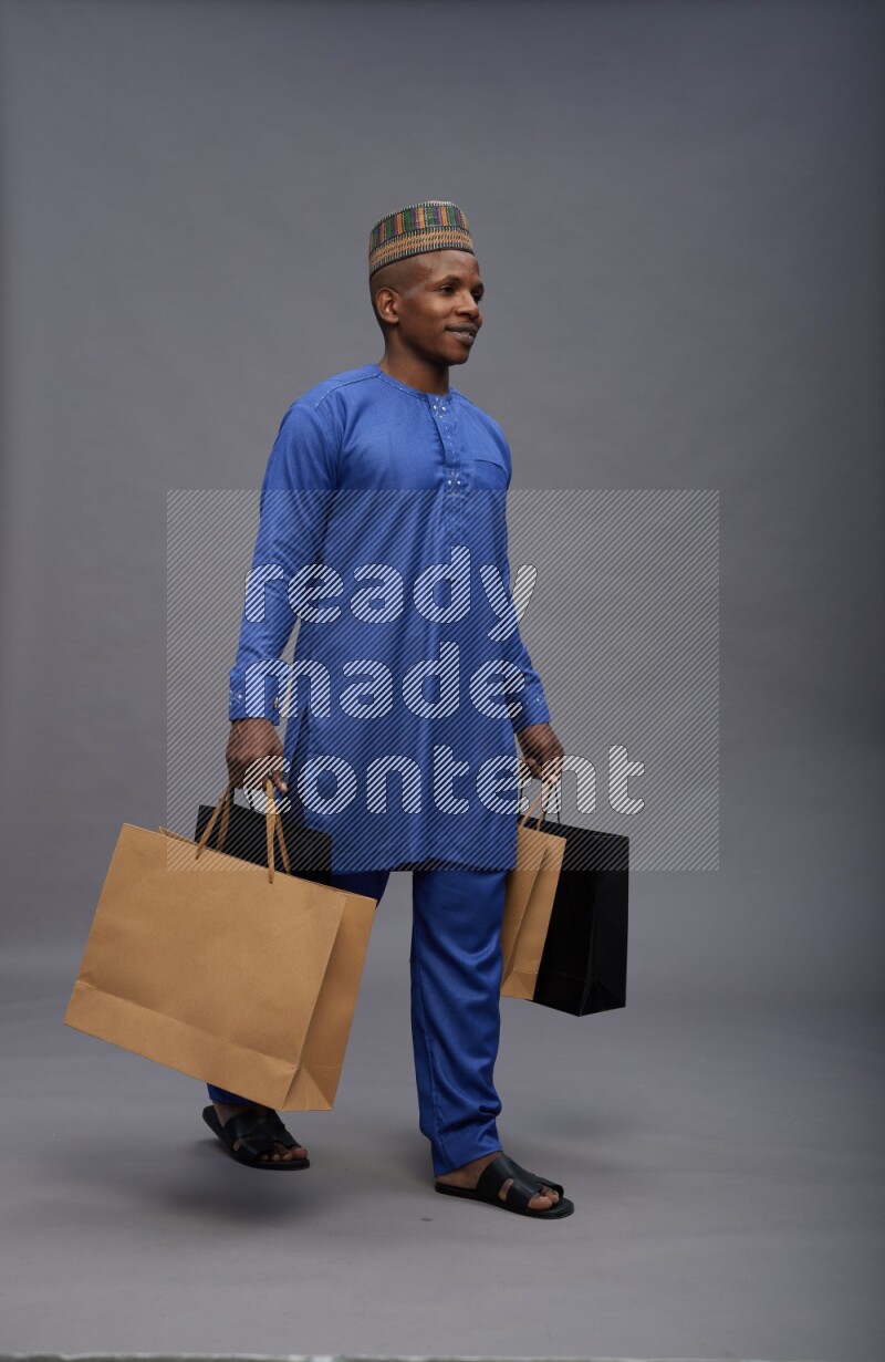 Man wearing Nigerian outfit standing holding shopping bag on gray background