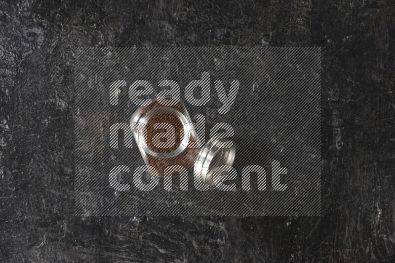 وعاء بهارات زجاجي ممتلئ ببودرة القرنفل على أرضية سوداء