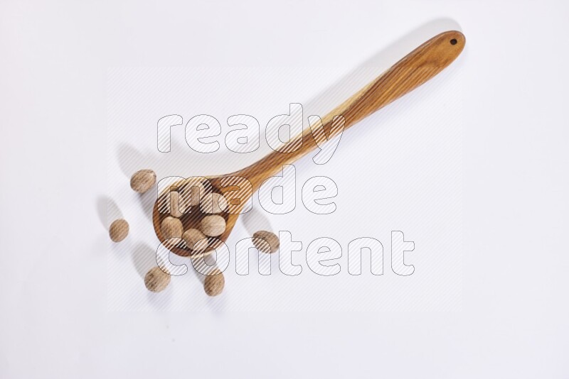A wooden ladle full of whole nutmeg seeds on a white flooring