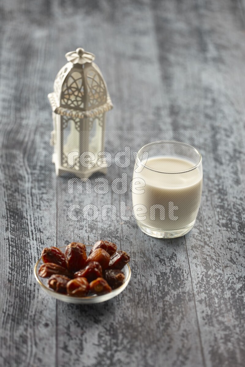 A white lantern with different drinks, dates, nuts, prayer beads and quran on grey wooden background