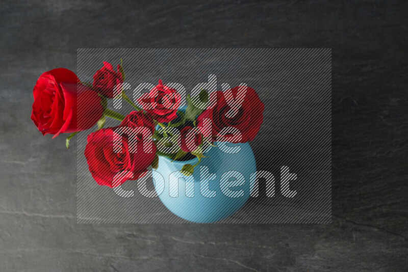 An arrangement of vivid red roses in a blue vase on black marble background