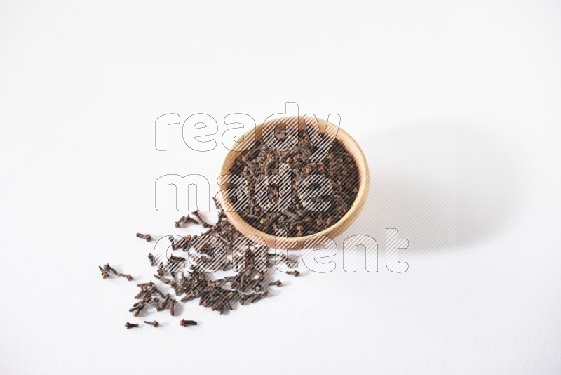 A wooden bowl full of cloves with spread grains on a white flooring