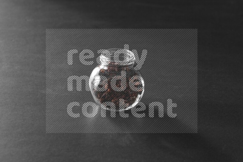 A glass spice jar full of cloves on black flooring
