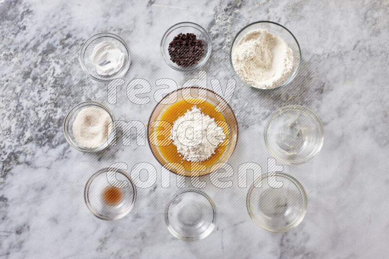 Cookies step by step with its ingredient, flour, butter, brown sugar, egg, vanilla extract, white sugar, chocolate chips and baking soda on grey marble background