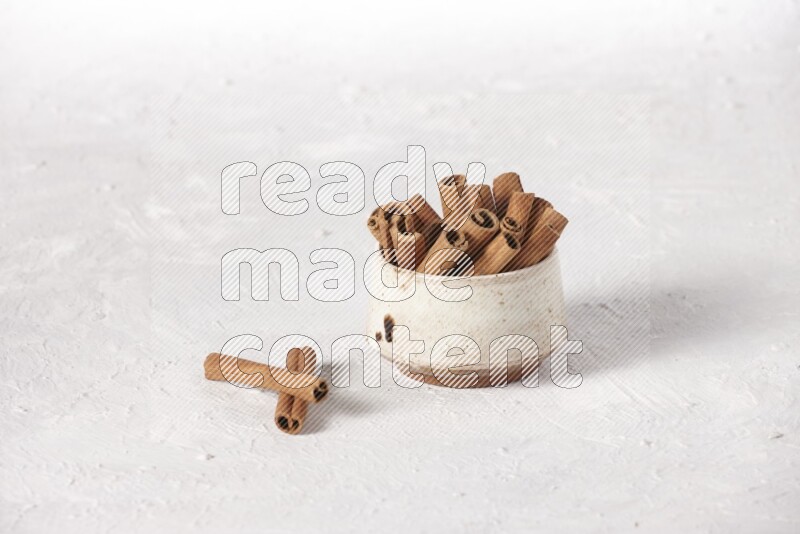 Cinnamon sticks in a beige bowl on a white background