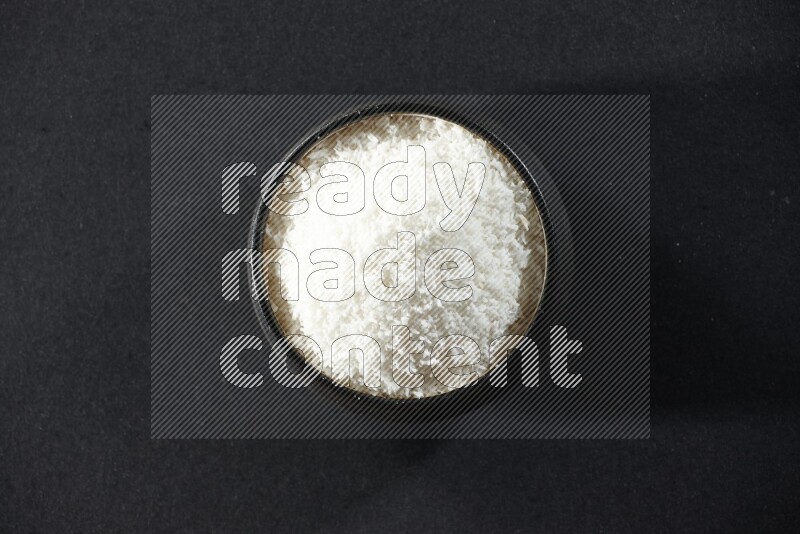 A black pottery bowl full of desiccated coconut on a black background in different angles