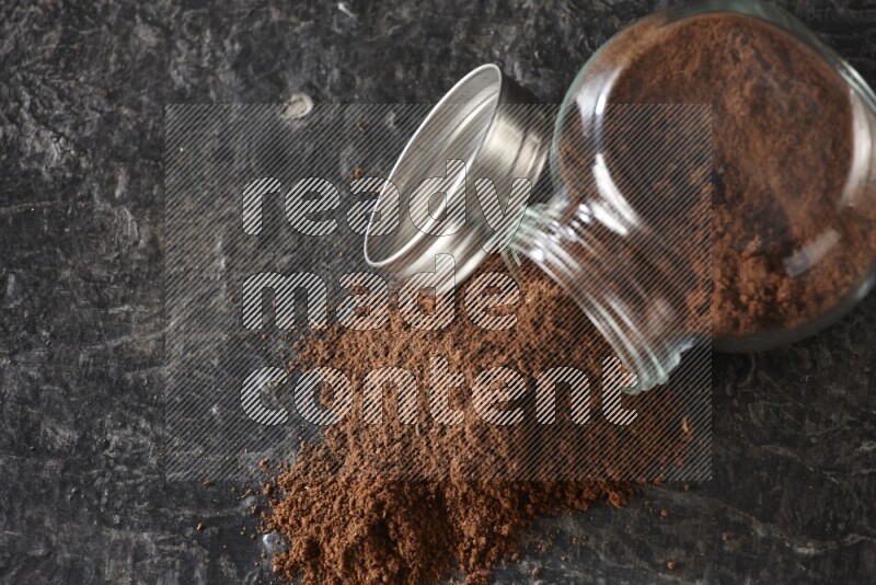 وعاء زجاجي للتوابل مقلوب ممتلئ ببودرة القرنفل والبودرة سقطت منه على أرضية سوداء