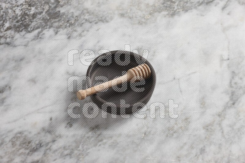 Black pottery bowl with wooden honey dipper in it on grey marble background