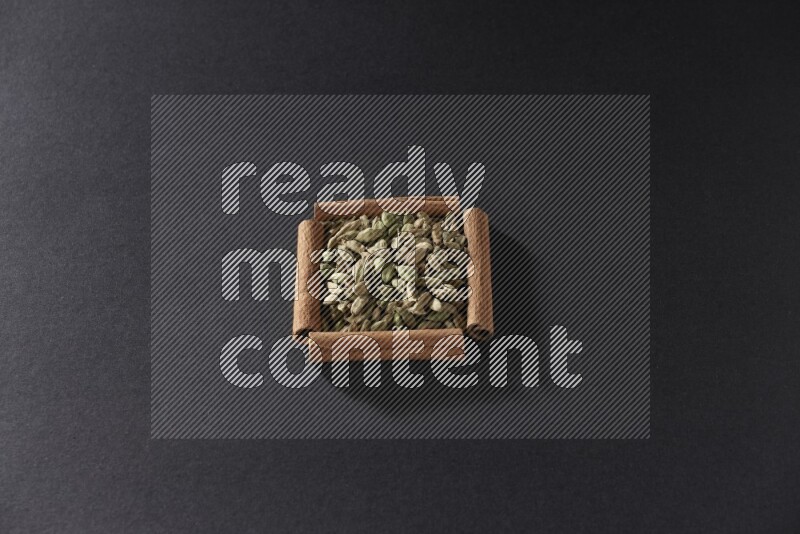 A single square of cinnamon sticks full of Cardamom on black flooring
