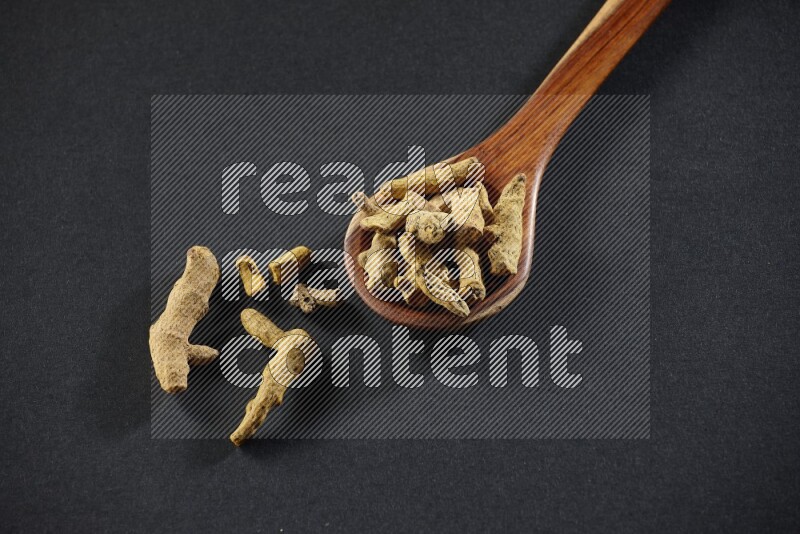 A wooden ladle full of dried turmeric fingers on black flooring