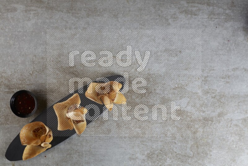wonton cups with soy sauce ramkin on oval slate on grey textured counter top