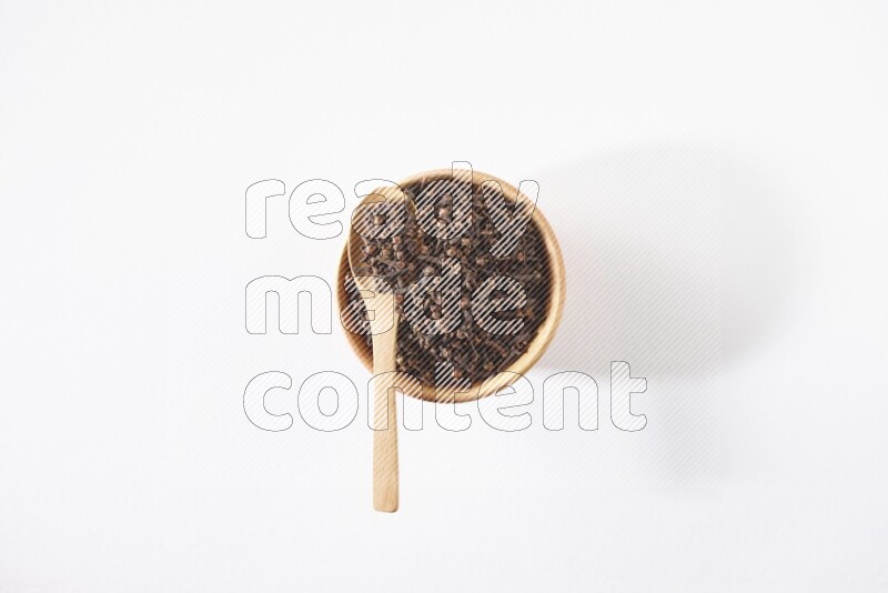 A wooden bowl and a wooden spoon full of cloves on a white flooring