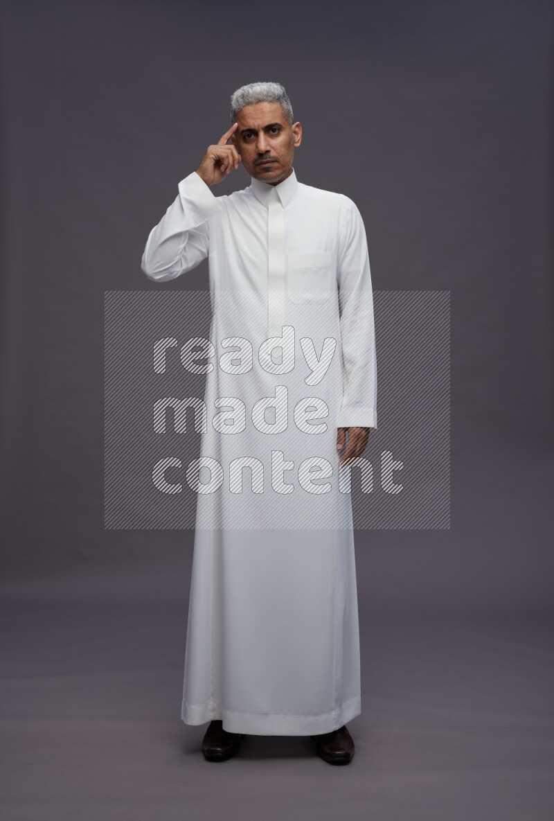 Saudi man wearing thob standing interacting with the camera on gray background