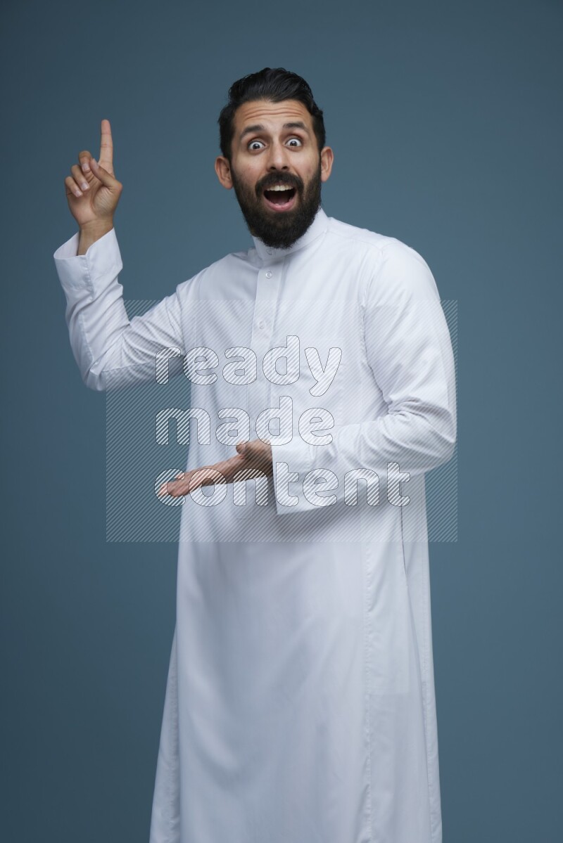 A man pointing in a blue background wearing Saudi Thob