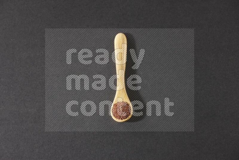 A wooden spoon full of garden cress seeds on a black flooring