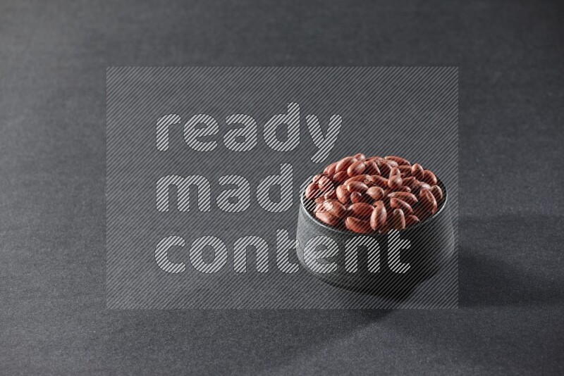 A black pottery bowl full of red skin peanuts on a black background in different angles