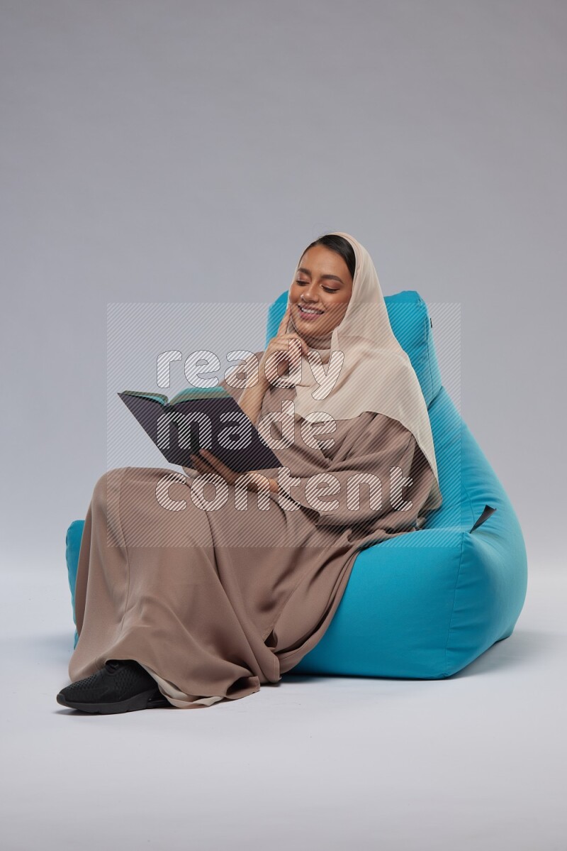 A woman sitting on a blue beanbag and reading a book