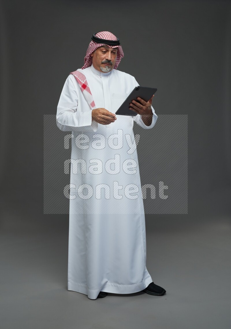 Saudi man with shomag Standing working on tablet on gray background