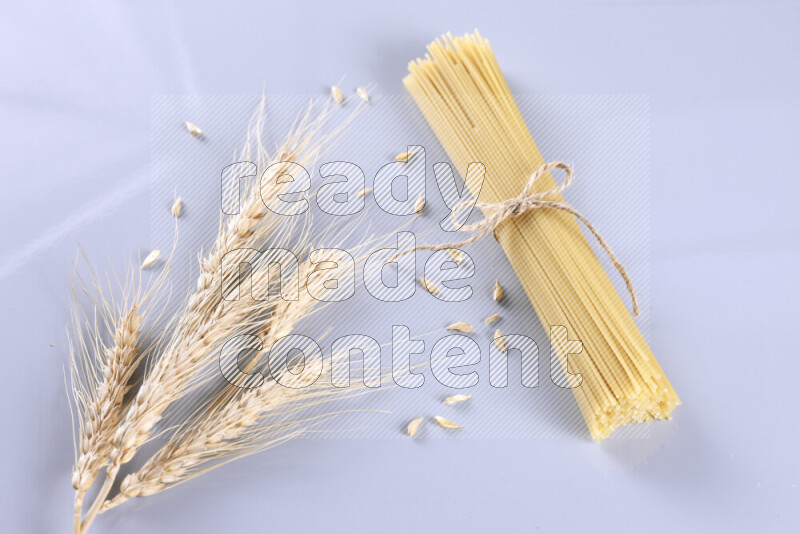 Raw pasta with wheat stalks on light blue background