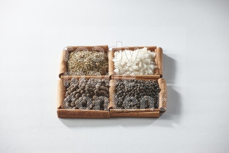 4 مربعات من أعواد القرفة ممتلئة بالكمون والملح الأبيض وبهار الفلفل الحلو وحبوب الفلفل الأسود على أرضية بيضاء