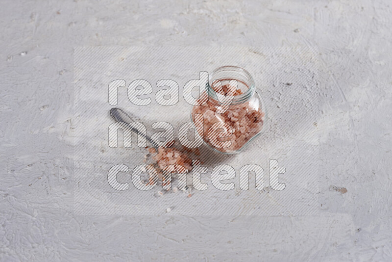 A glass jar full of coarse himalayan salt crystals on white background