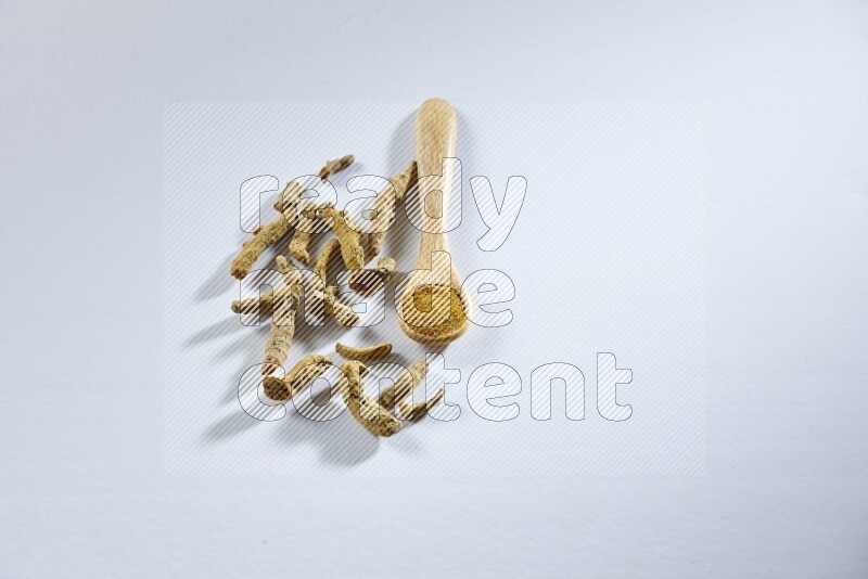A wooden spoon full of turmeric powder with dried turmeric fingers beside it on white flooring