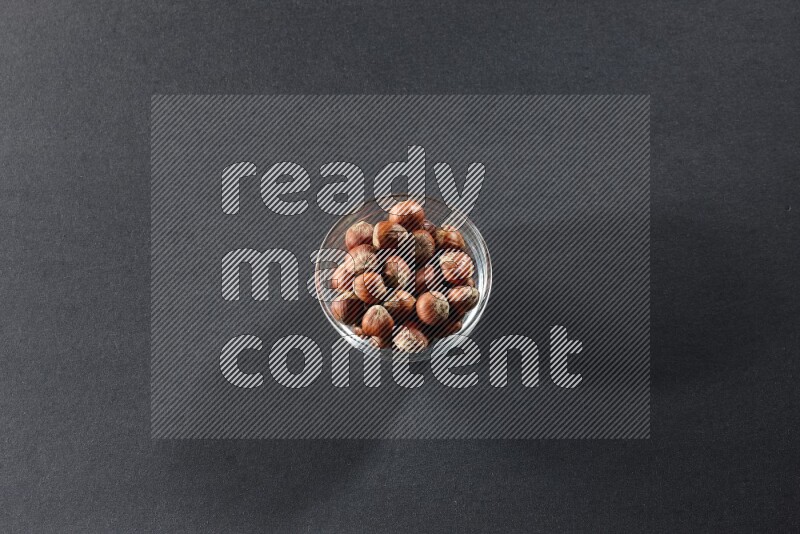 A glass bowl full of hazelnuts on a black background in different angles