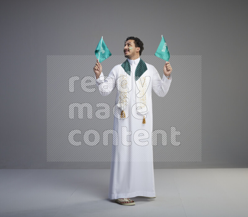 رجل سعودي يرتدي ثوب ابيض ويحمل علم السعودية