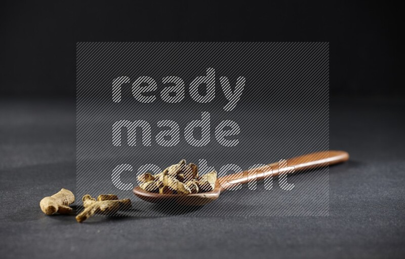 مغرفة خشبية ممتلئة بأصابع الكركم المجففة على خلفية سوداء