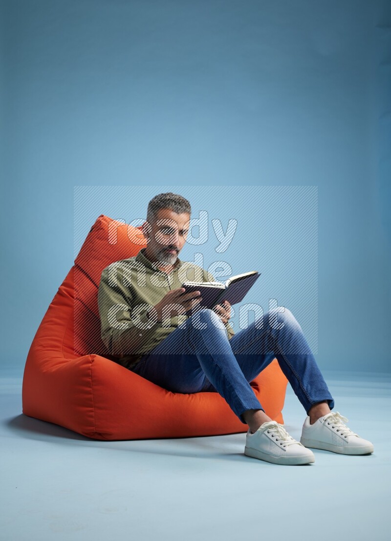 A man sitting on an orange beanbag and reading a book