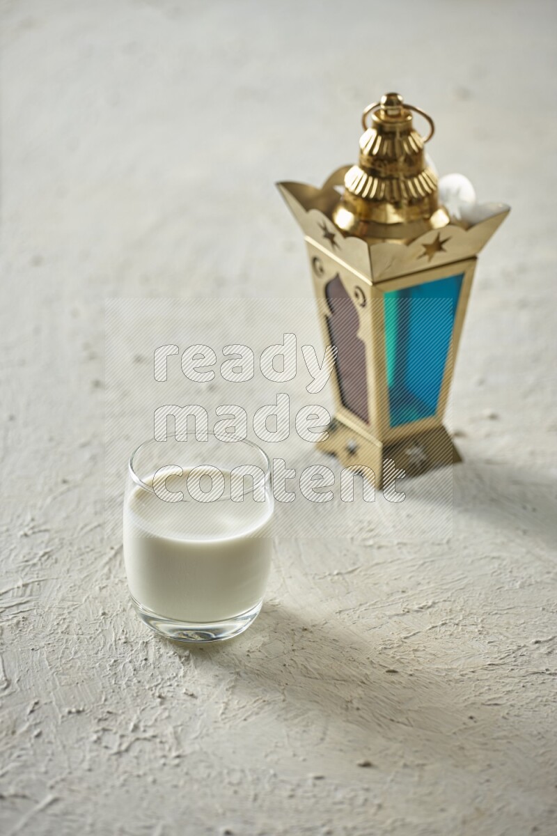 A golden lantern with different drinks, dates, nuts, prayer beads and quran on textured white background