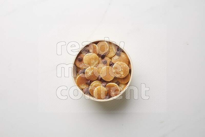 Top-view shot of chocolate chips cereal pancakes in a round bowl on white background