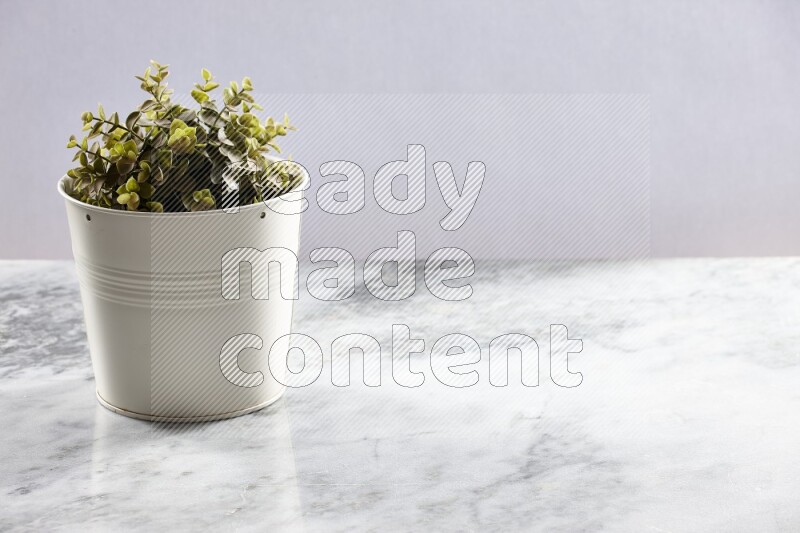 Green artificial plant in white pot on light grey marble background
