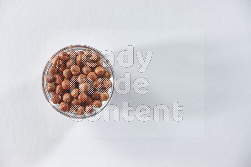 A glass bowl full of peeled hazelnuts on a white background in different angles