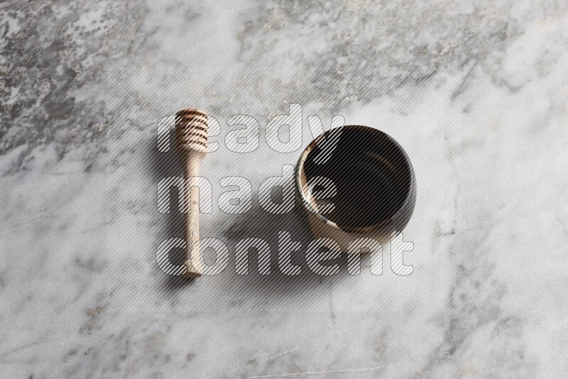 Multicolored pottery bowl with wooden honey dipper on the side on grey marble background