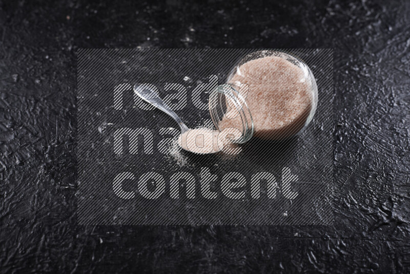 A glass jar full of fine himalayan salt on black background