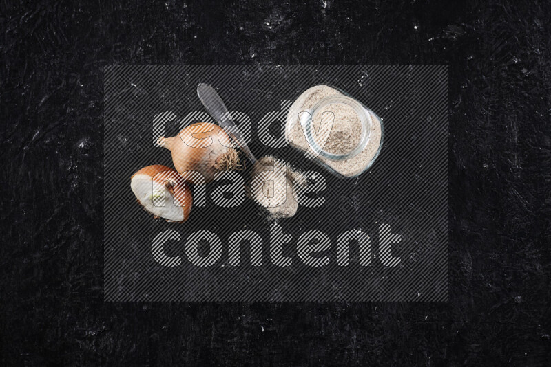 A glass jar full of onion powder on black background