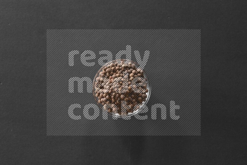 A glass bowl full of allspice on black flooring