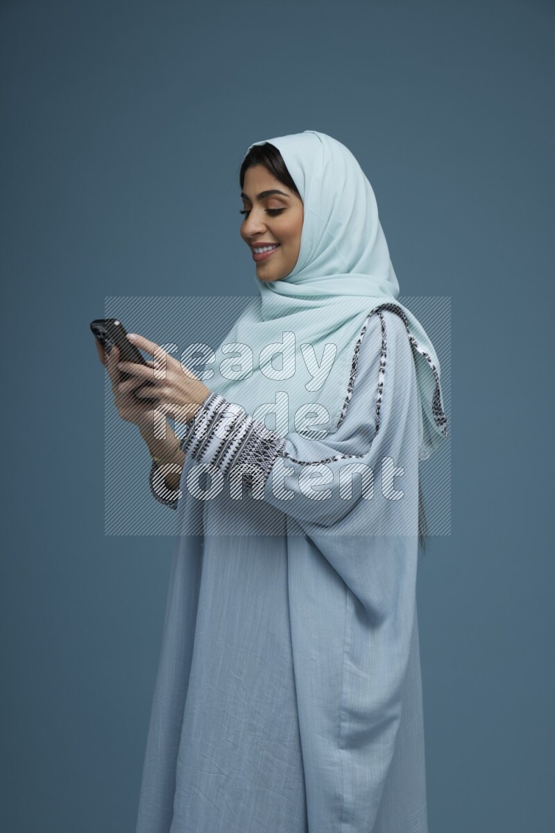A Saudi woman Texting in a blue background wearing a blue Abaya with hijab