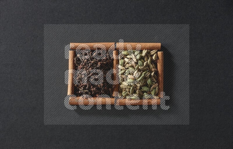 مربعان من أعواد القرفة ممتلئان بحبوب الهيل والقرنفل علي خلفية سوداء