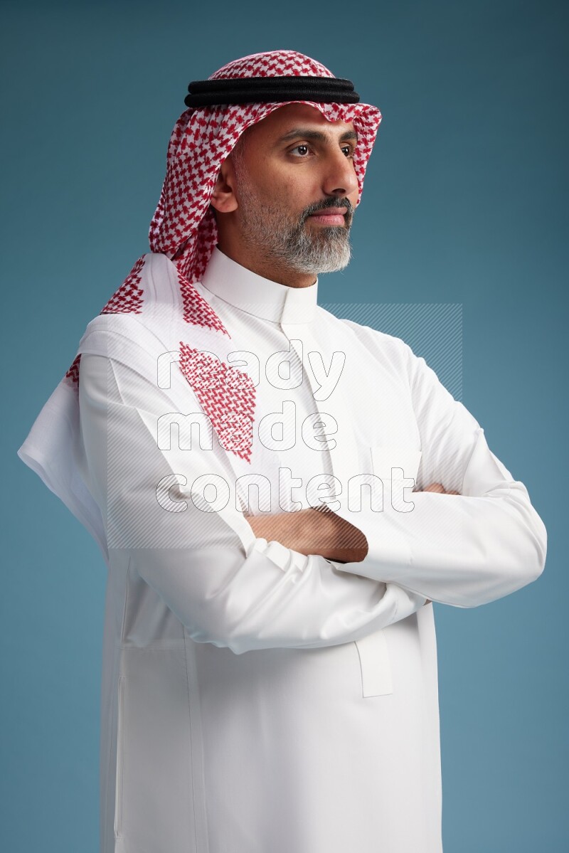 Saudi man wearing thob and shomagh posing to the camera on blue background