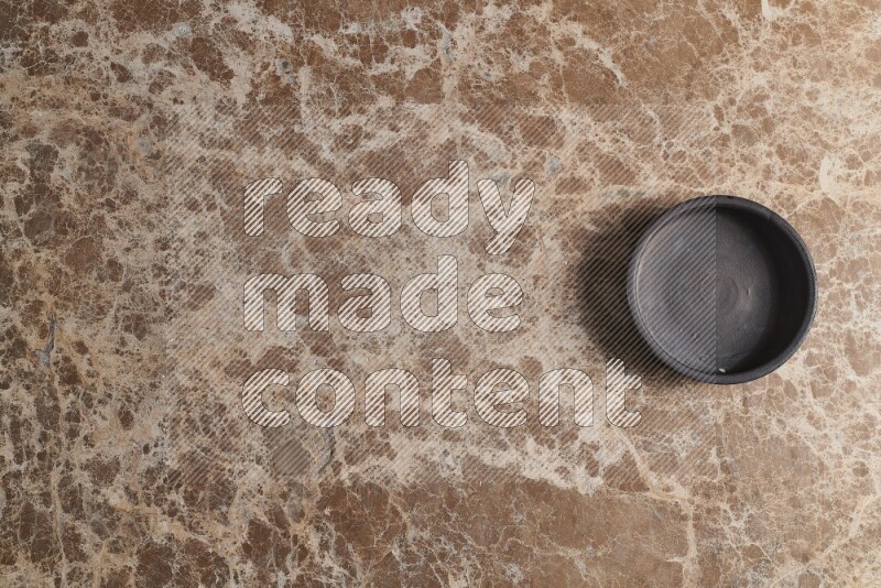 A black pottery bowl on beige marble background