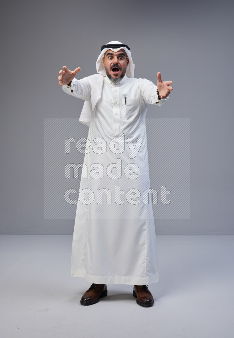 Saudi man Wearing Thob and white Shomag standing interacting with the camera on Gray background