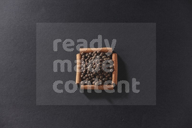 A single square of cinnamon sticks full of allspice on black flooring